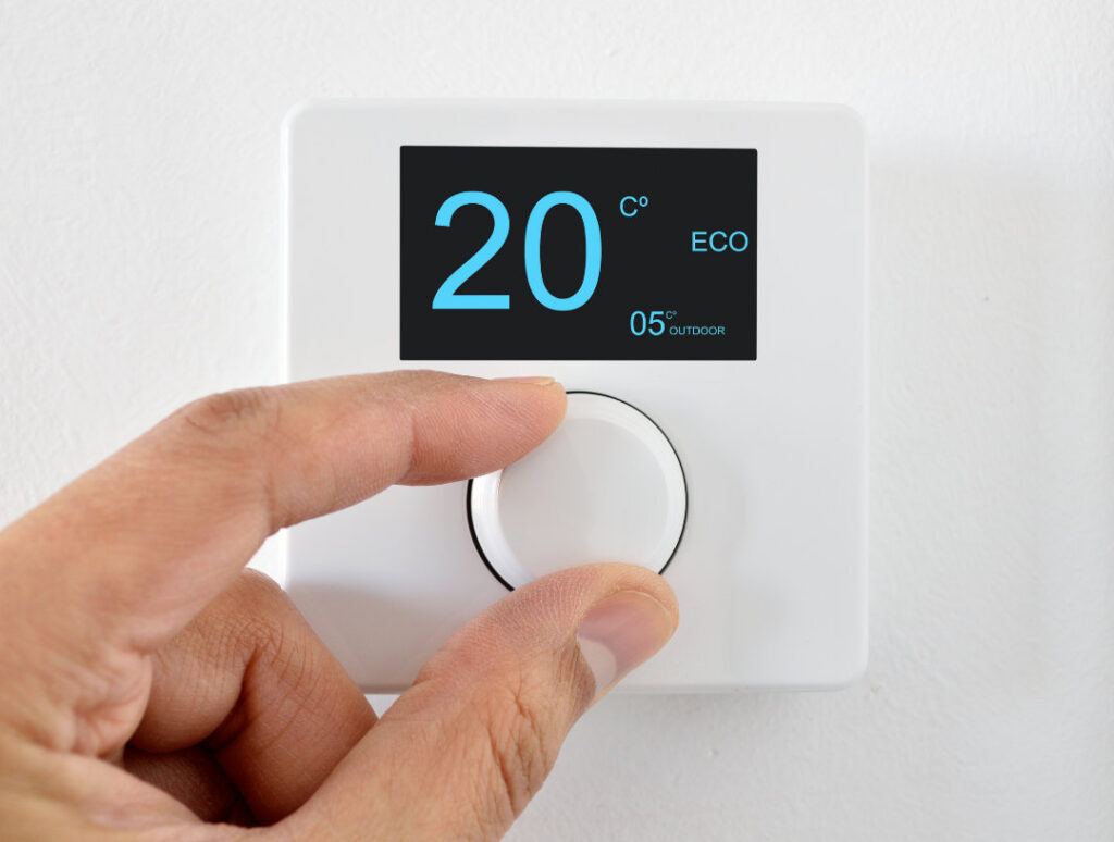 Foto für Blog Beitrag ELHADO Im Winter richtig heizen. Menschliche Hand dreht an digitalem Thermostat und stellt es auf 20°C ein