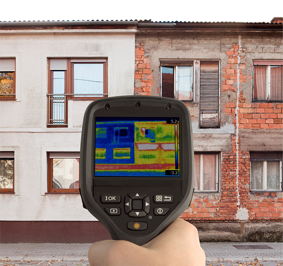 Vorteile Thermografie Foto - Hand hält Wärmebildkamera vor Doppelhaus. Eine hälfte des Hauses ist saniert, die andere ist in schlechtem Zustand. Man sieht auf der Wärmebildkamera klar den Unterschied zwischen der Energieeffizienz beider Gebäudeteile.