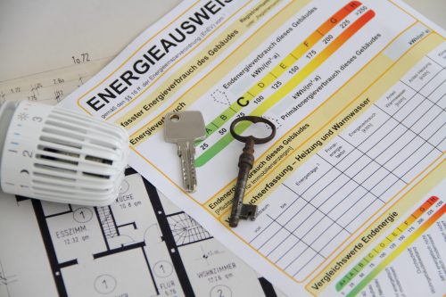 Bild über Energieausweis erstellen. Energieausweis liegt auf Tisch. Darauf liegen zwei Schlüssel. Daneben ein Heizungsthermonstat und darunter ein Hausplan.